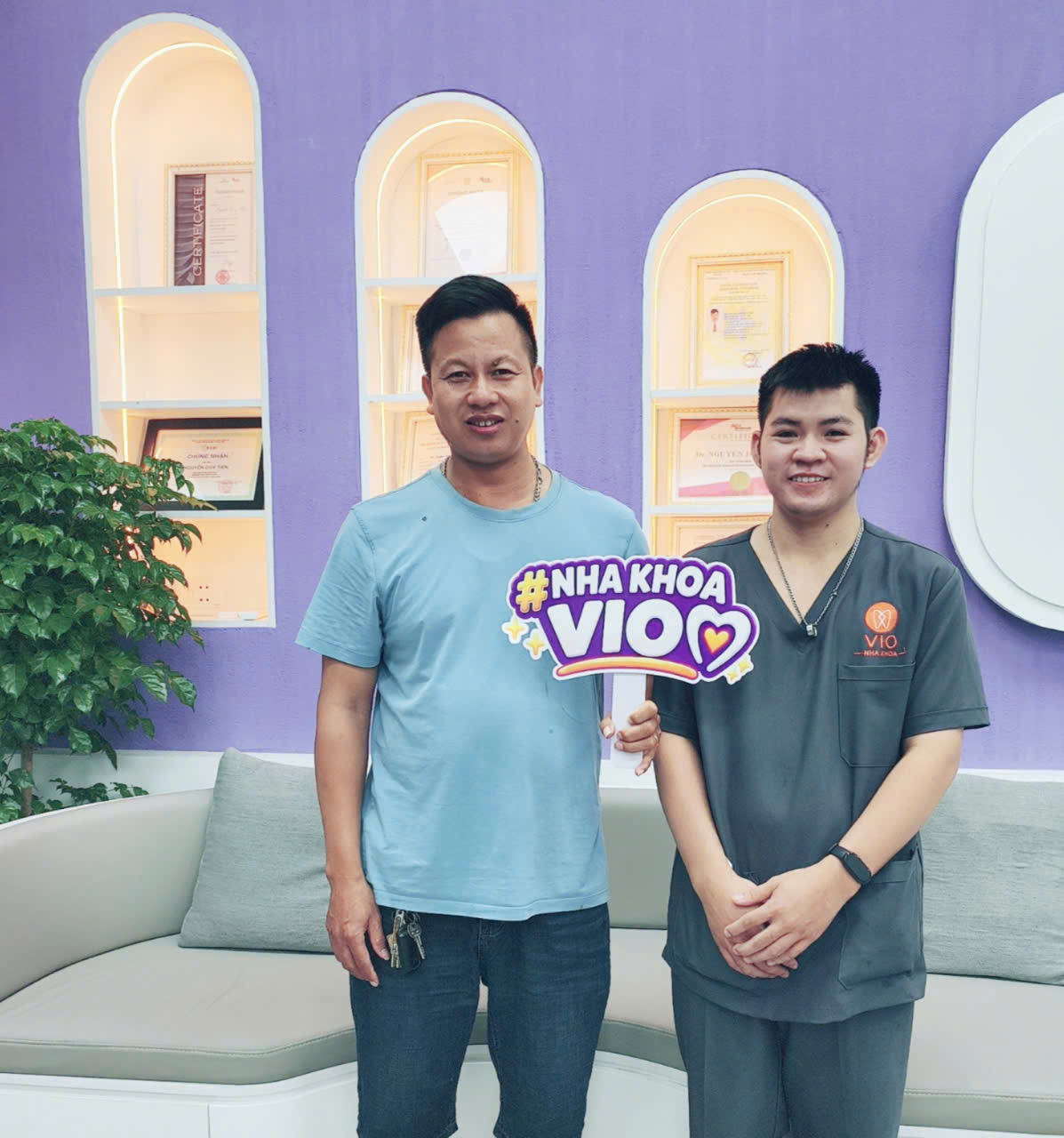 Khách hàng cầm bảng #NhaKhoaVIO cùng nhân viên VIO